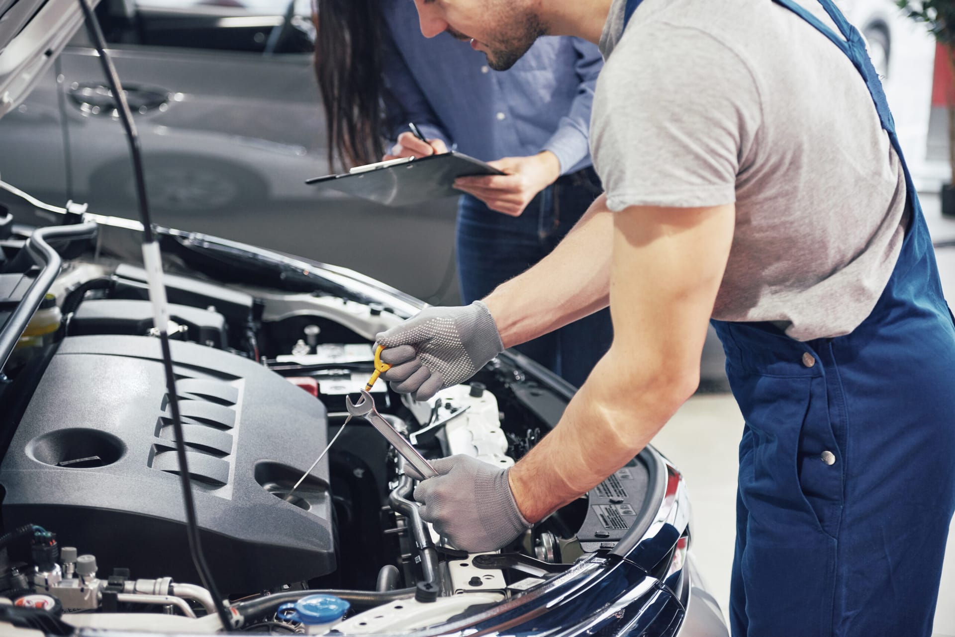 A man mechanic and woman customer look at the car hood and discuss repairs.